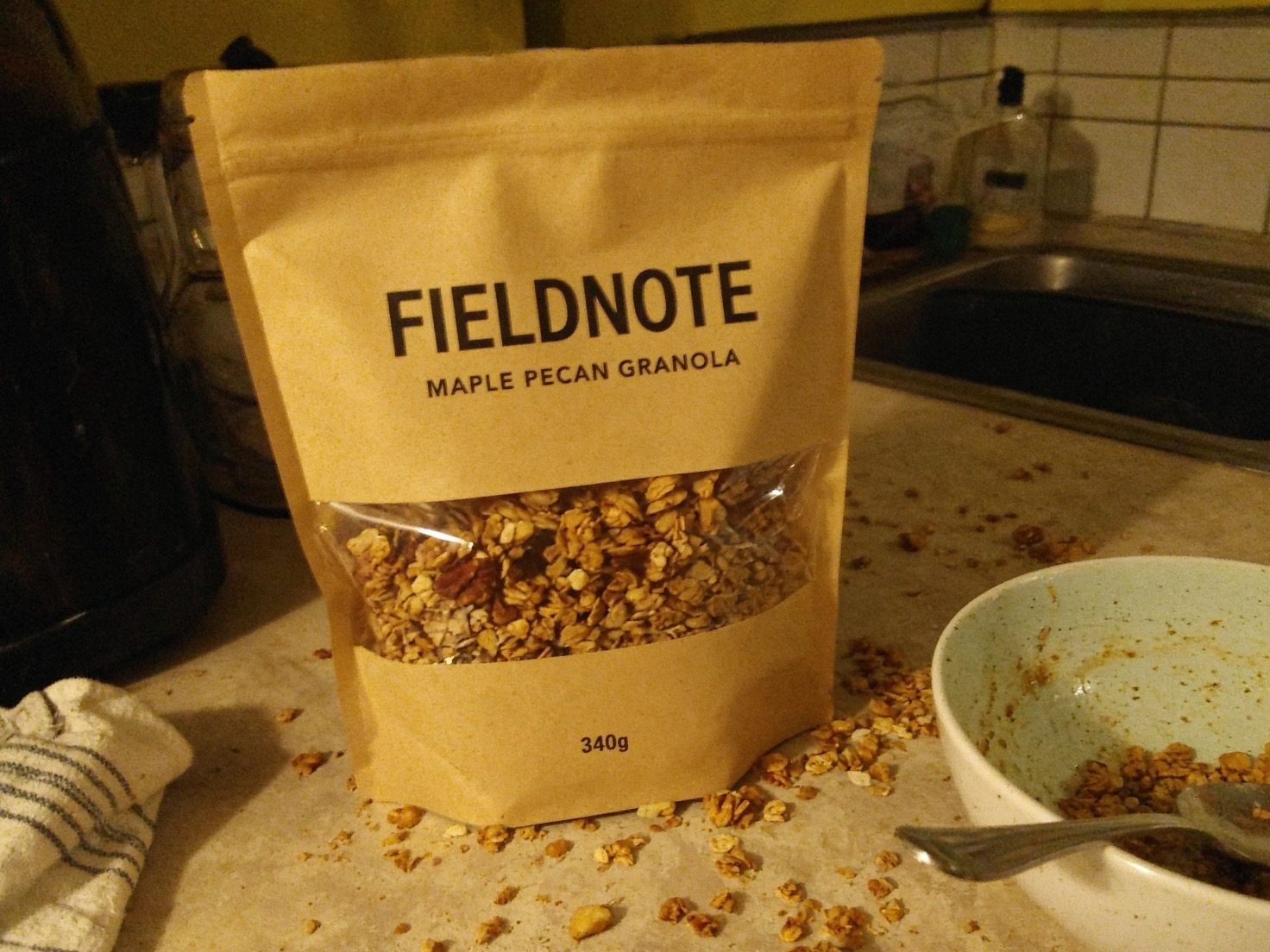 The source photo: a kraft granola pouch on a cluttered kitchen counter at night