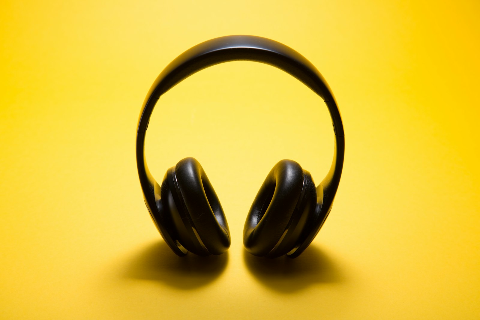 Finished hero packshot: black wireless headphones standing on a vivid yellow studio backdrop