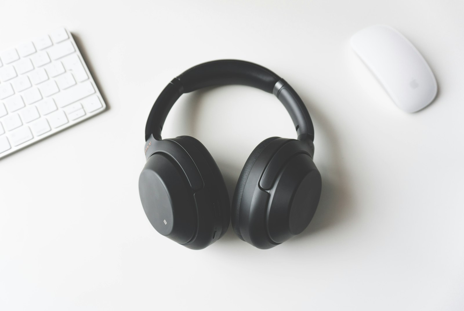 Generated lifestyle scene: the same headphones on a white desk between keyboard and mouse