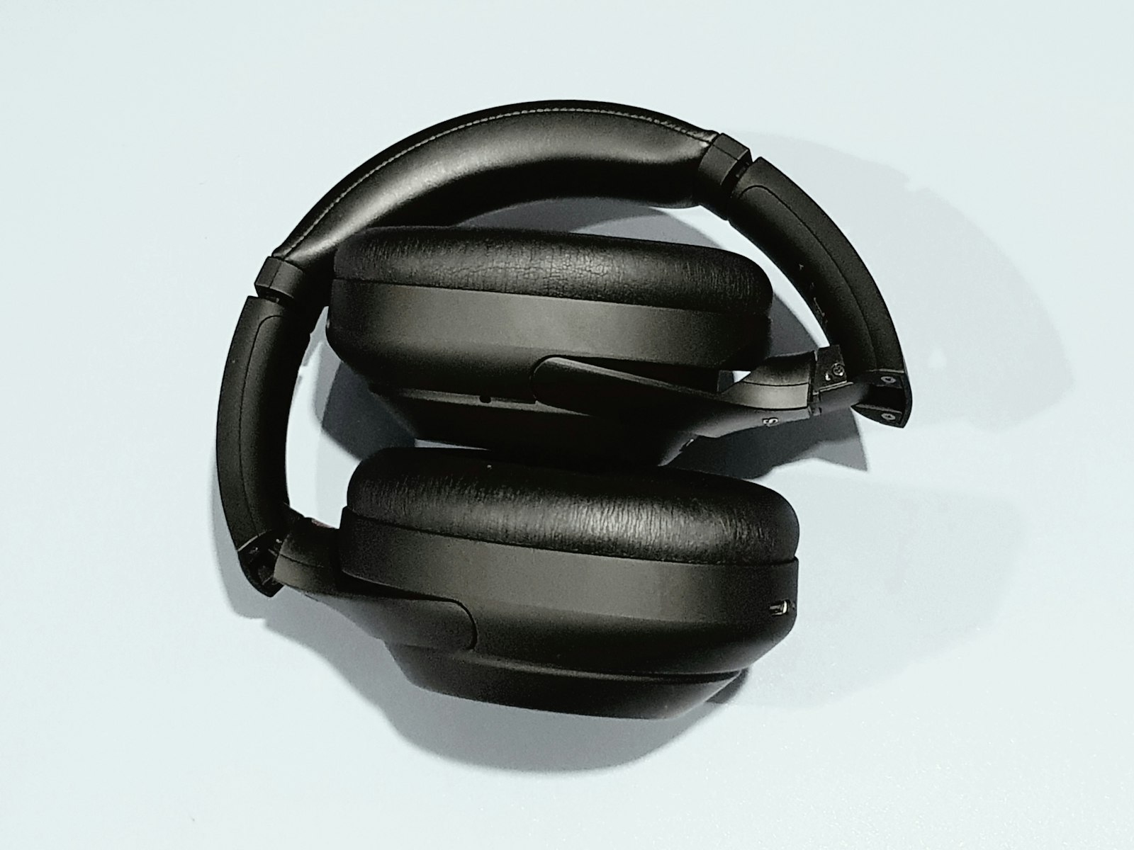 Generated studio scene: the headphones folded under hard light on a pale blue surface