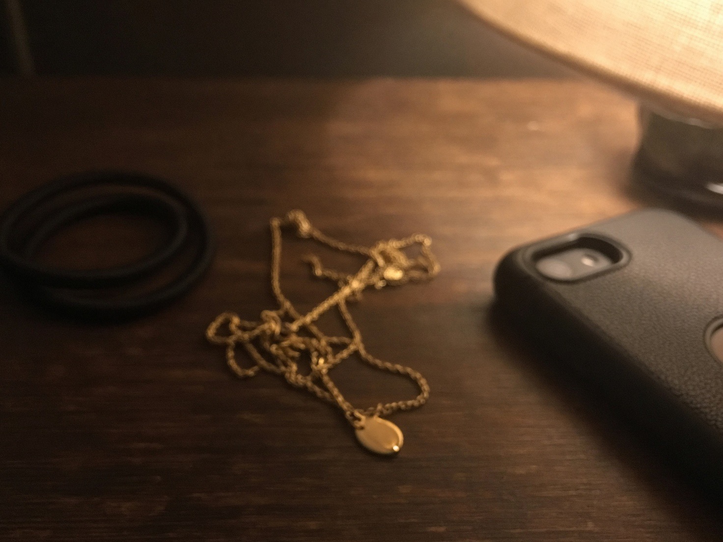 Phone photo: a gold pendant necklace tangled on a dark dresser