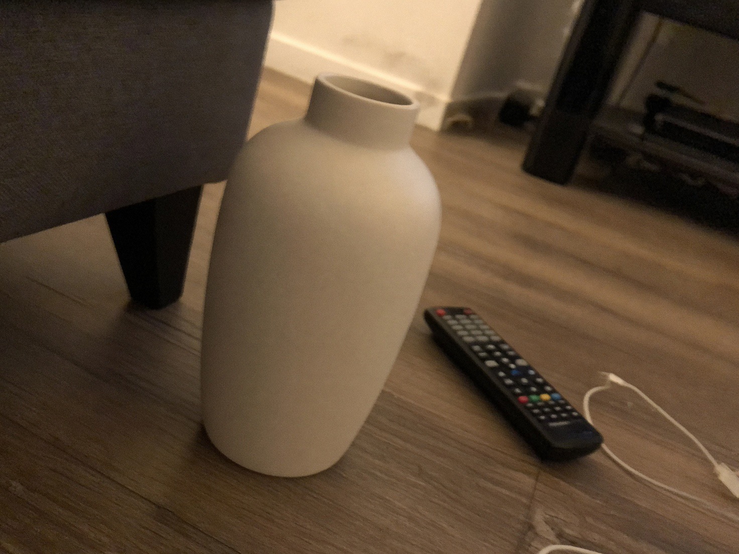 Phone photo: a white ceramic vase on the floor beside a TV remote